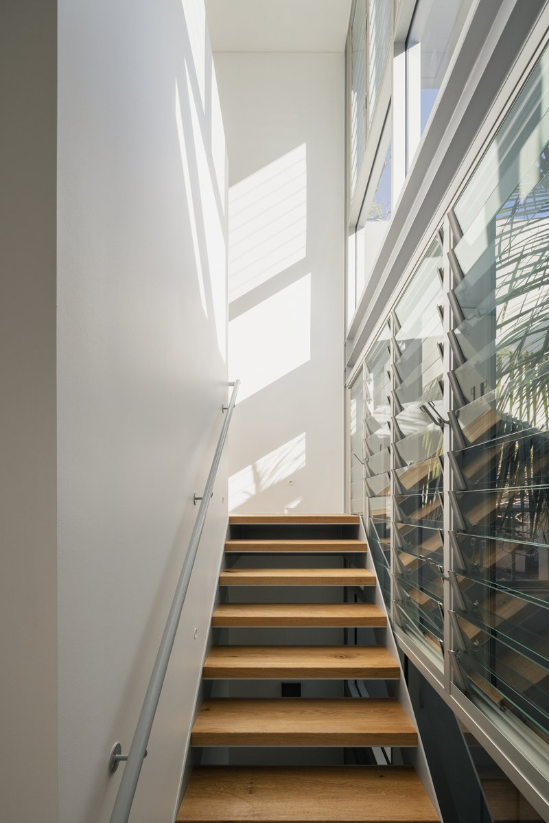 Timber-tread staircase with steel stringers alongside glazed louvered windows casting shadows