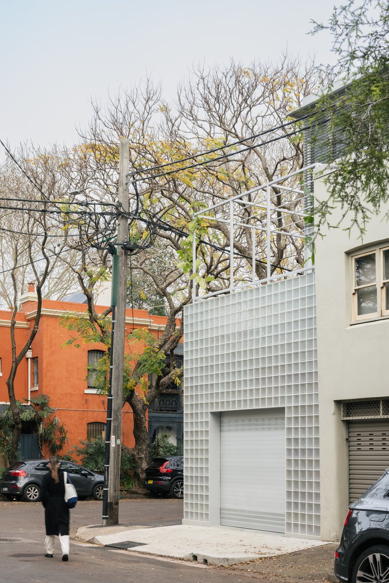 Street facade with glass block cladding wrapping around the corner beneath bare winter trees