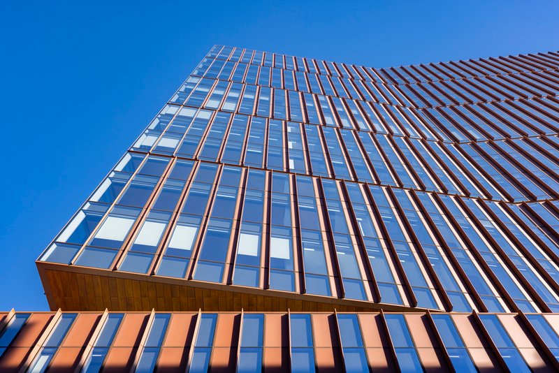 Upward view of the glazed tower facade with bronze vertical fins against a clear blue sky