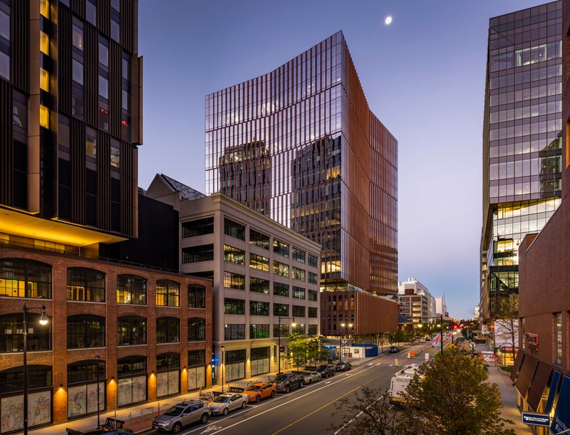 Street view of the tower rising above neighboring buildings at dusk with a crescent moon overhead