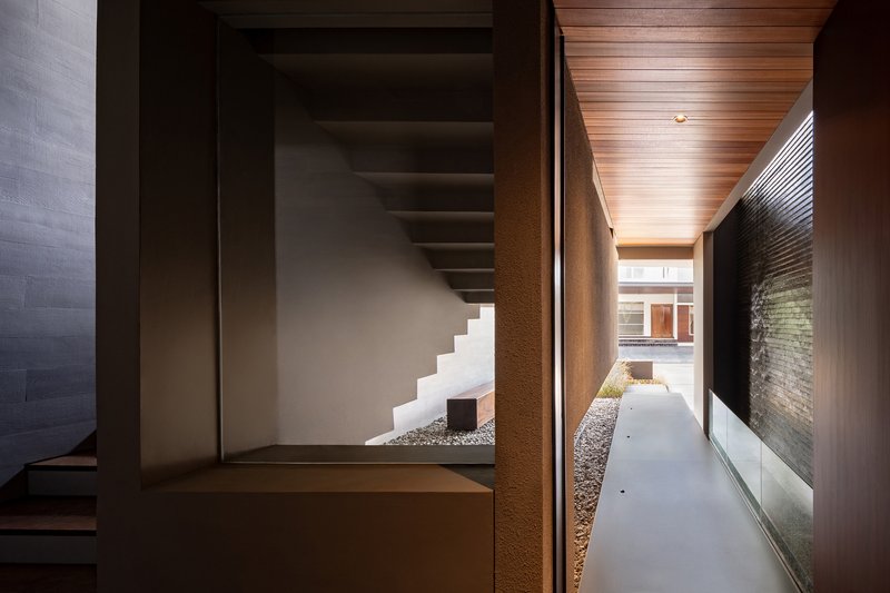 Interior corridor with timber ceiling looking toward courtyard stair and gravel bed through glass walls