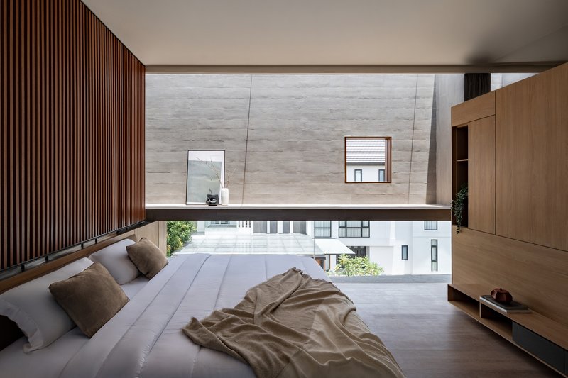 Bedroom with timber slat wall and horizontal window band framing the perforated facade of the neighboring structure