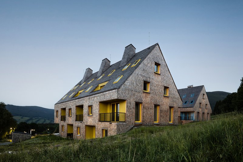 Shingled facade with yellow-framed windows and dormers illuminated at twilight on a hillside
