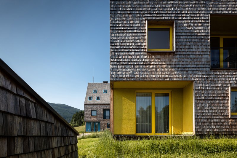 Yellow balcony projection with glass doors set into weathered timber shingle wall