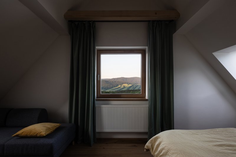 Bedroom window with dark curtains framing a view of the forested hills at dusk