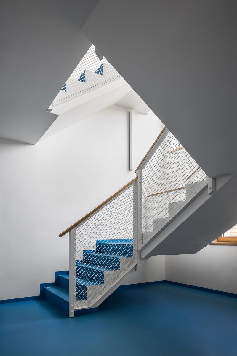 Interior staircase with blue treads and mesh infill under a peaked skylight