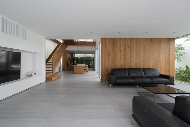 Double-height living room with timber staircase and large-format grey floor tiles beneath a white ceiling