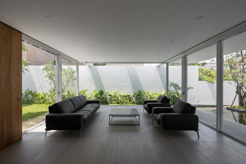 Living room with floor-to-ceiling glazing overlooking planted courtyard garden under overcast sky