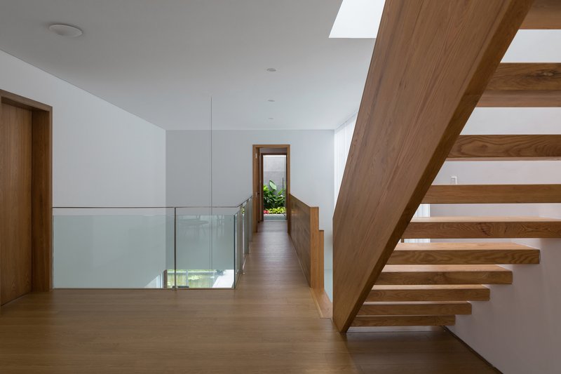 Upper level hallway with cantilevered timber staircase, glass guardrail, and skylights overhead