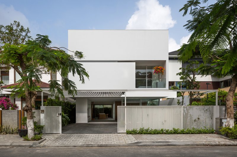 Street view of white stucco facade with vertical slatted fence and cantilevered upper volume beneath tropical trees
