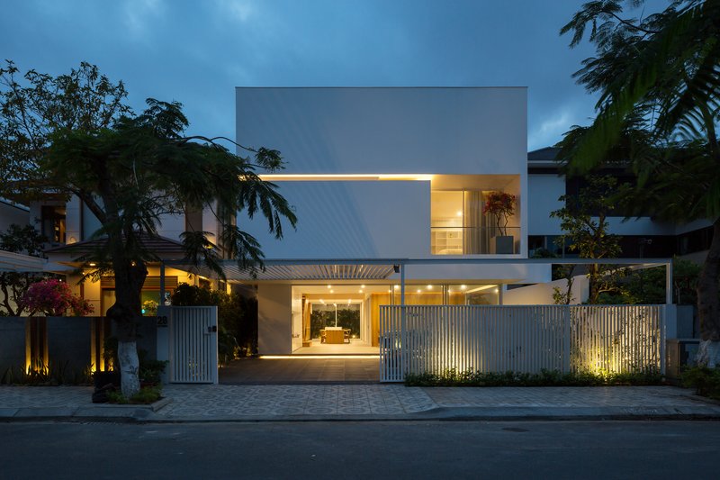 Street facade at twilight showing vertical slatted fence, recessed carport, and illuminated upper balcony