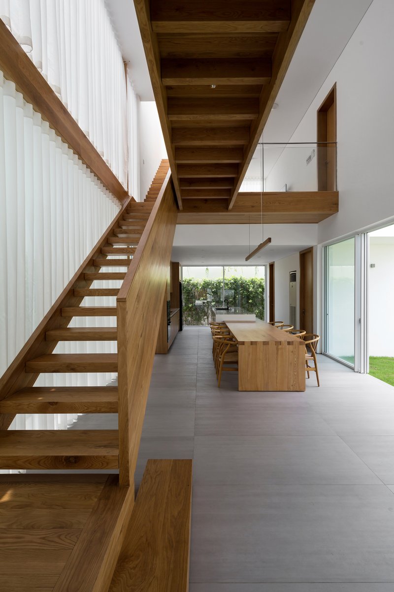 Open-tread timber staircase rising beside the dining area with glazed balustrade at the upper level