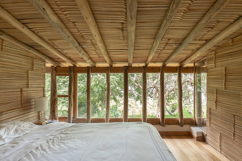 Bedroom with bamboo slat ceiling and walls, floor-to-ceiling glazed doors opening to greenery beyond