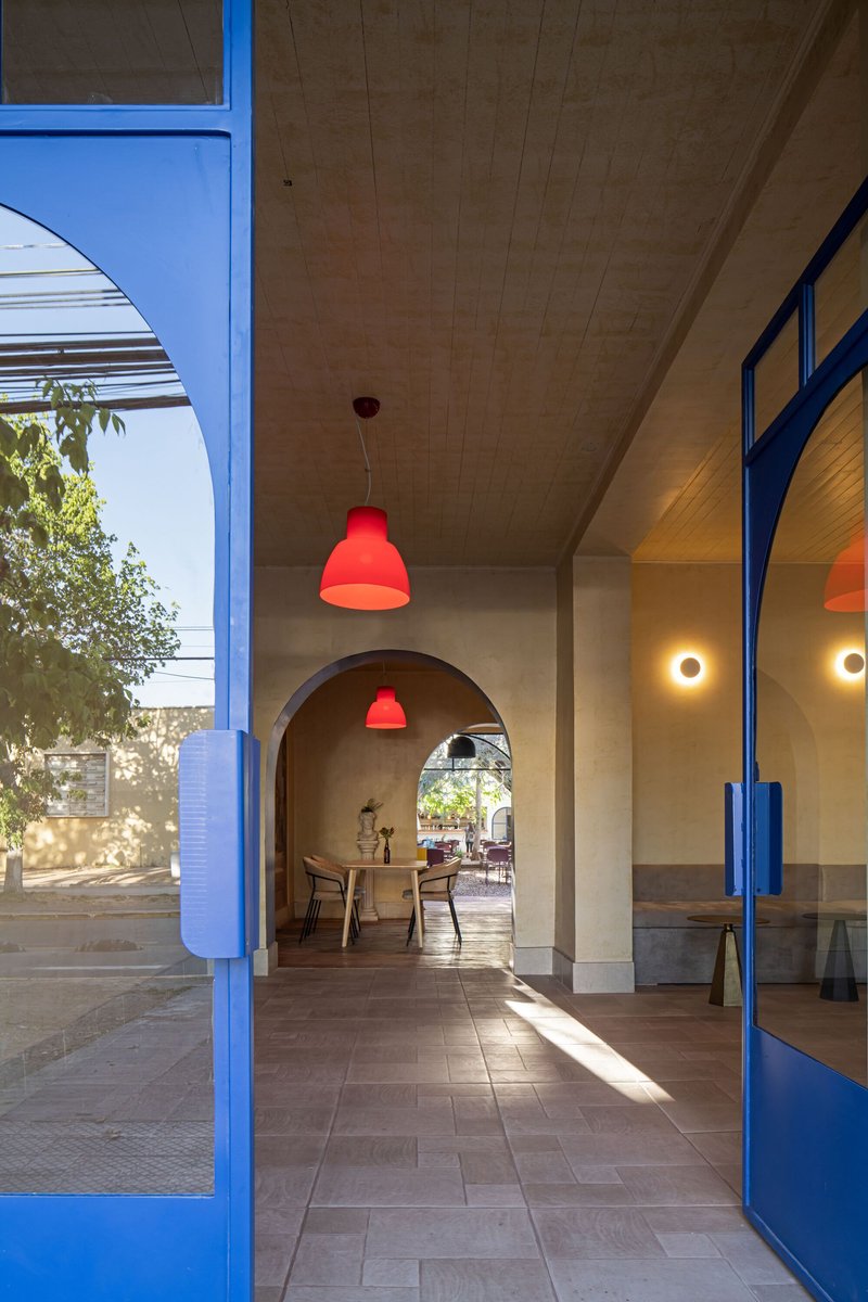Arched corridor with blue steel framed doors and red pendant lights in afternoon sunlight