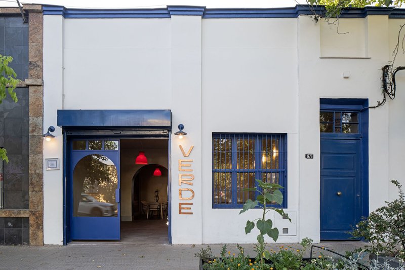 White stucco street facade with blue painted steel frames and arched doorway at twilight
