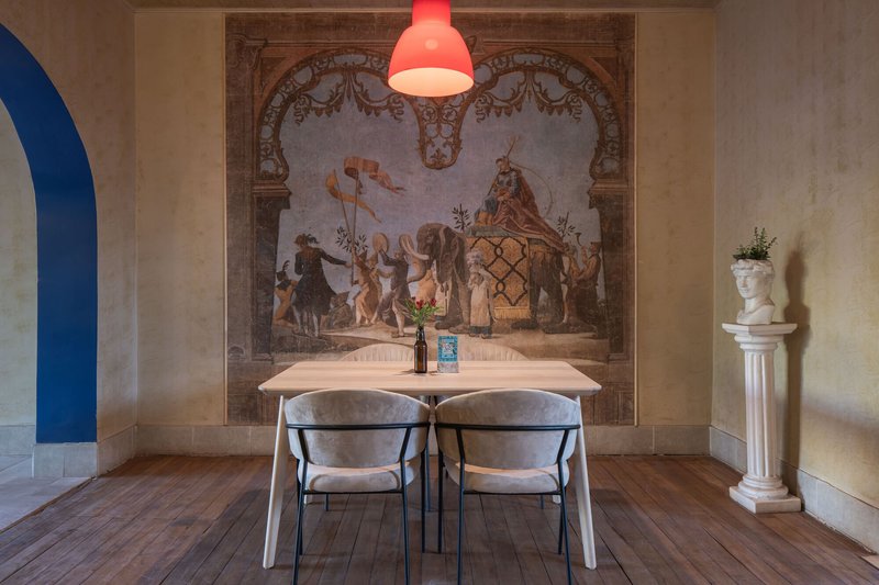 Dining alcove with faded fresco wall mural and red pendant light above timber floor