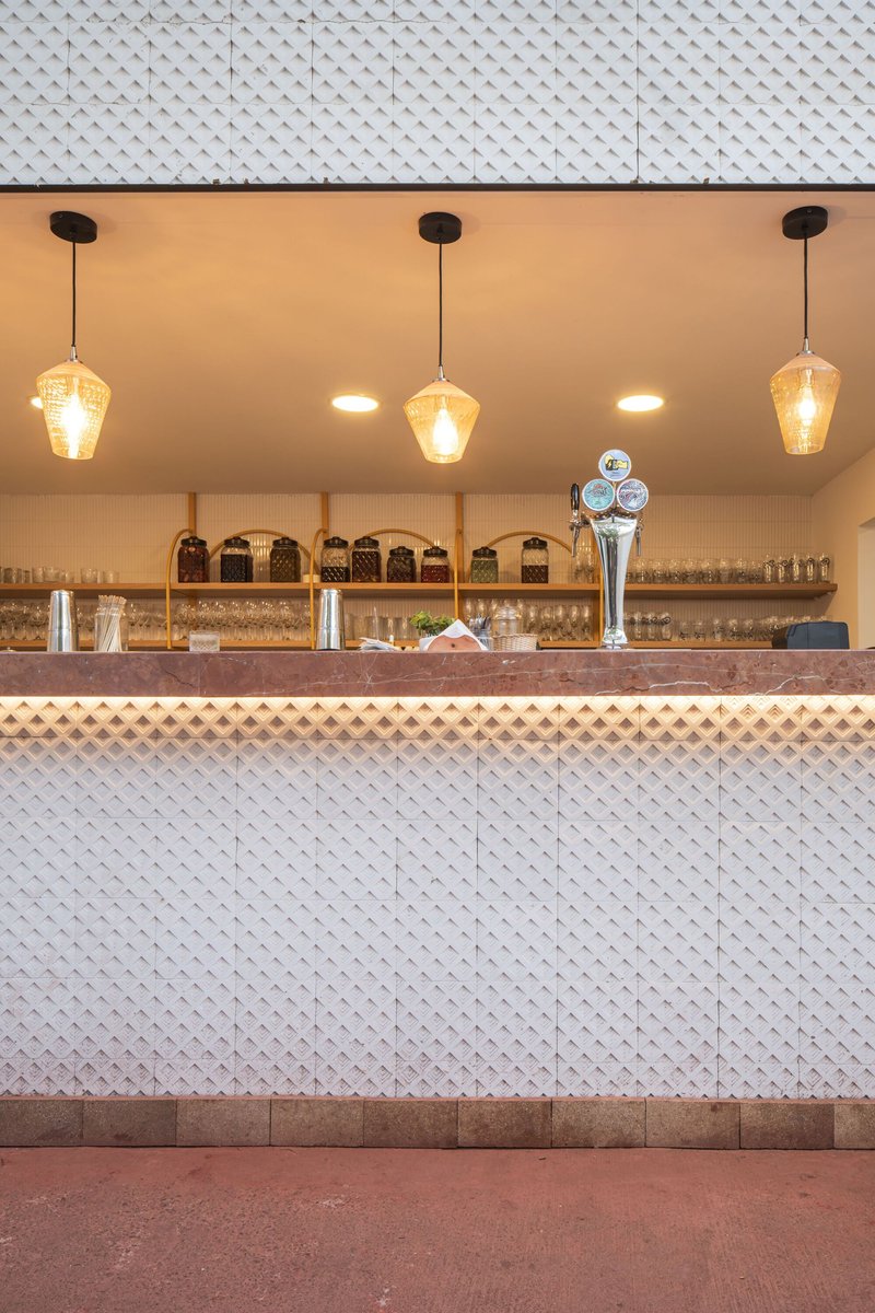 Bar counter with white diamond-patterned tile cladding and three amber pendant lights above