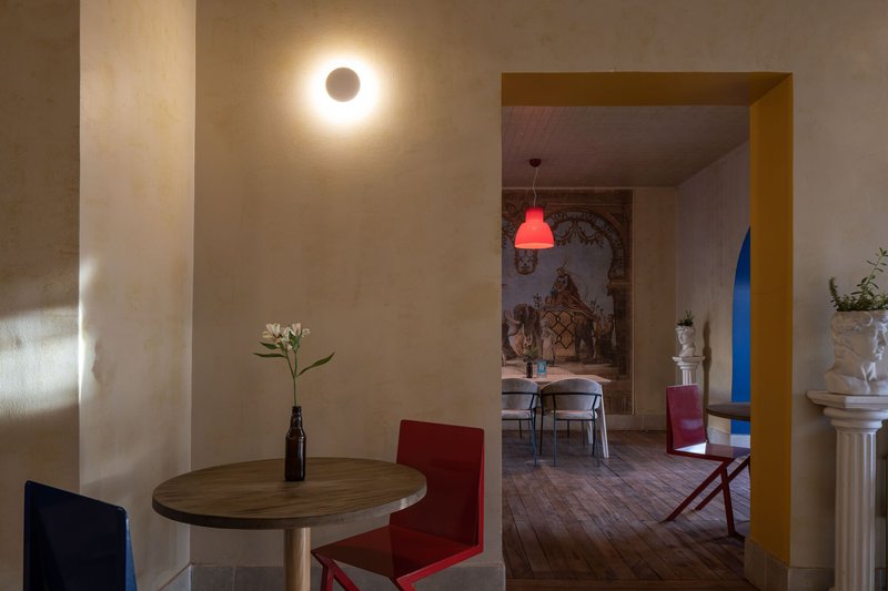 Interior view through a yellow-framed doorway connecting two dining spaces with circular wall sconces
