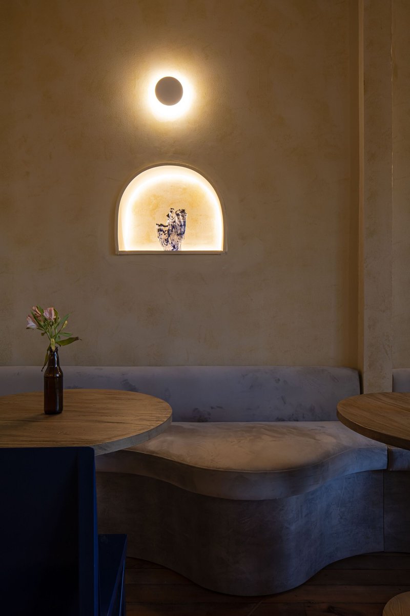 Corner banquette seating with curved concrete bench and arched wall niche lit from within