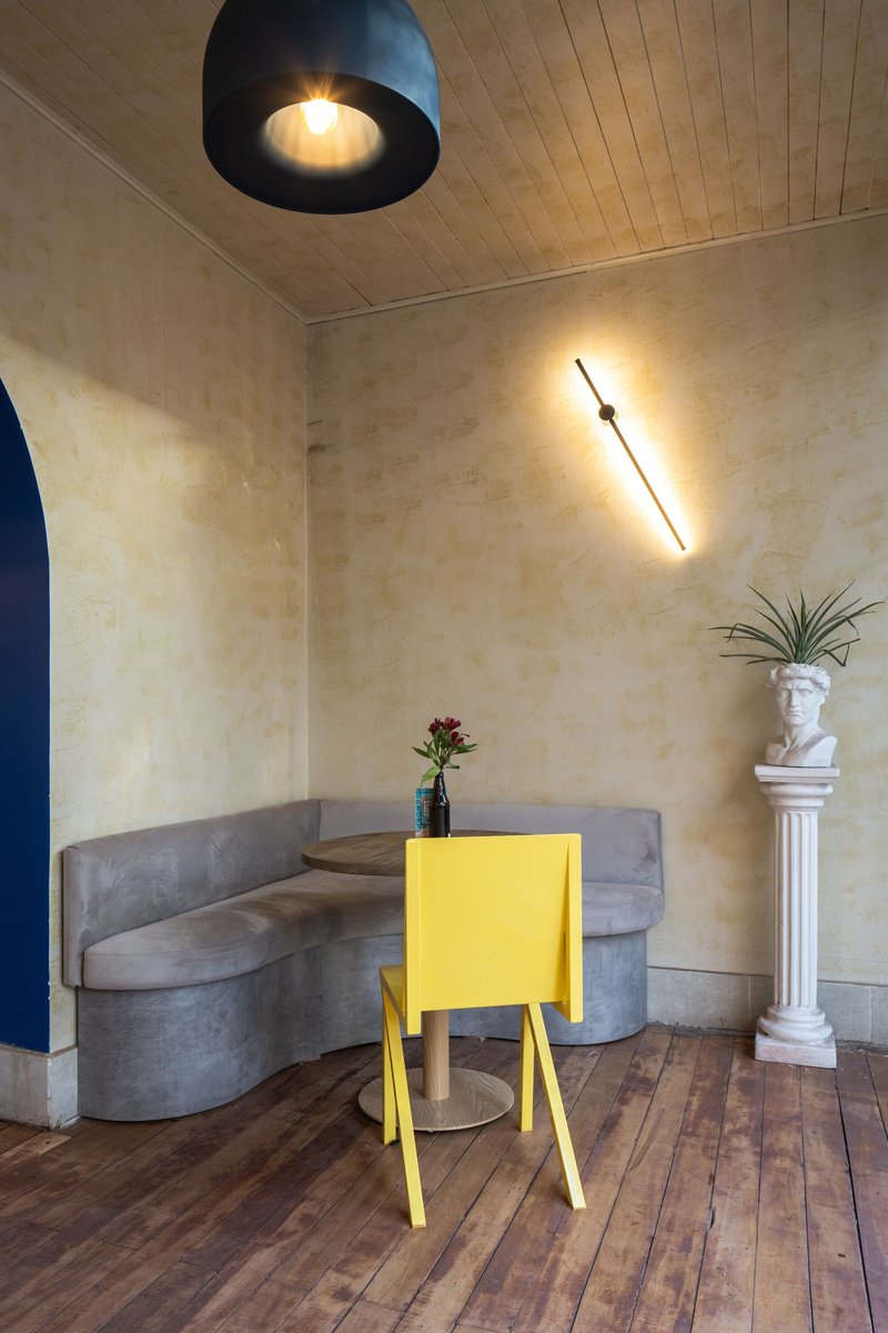 Curved concrete banquette with yellow side table and diagonal wall-mounted light fixture