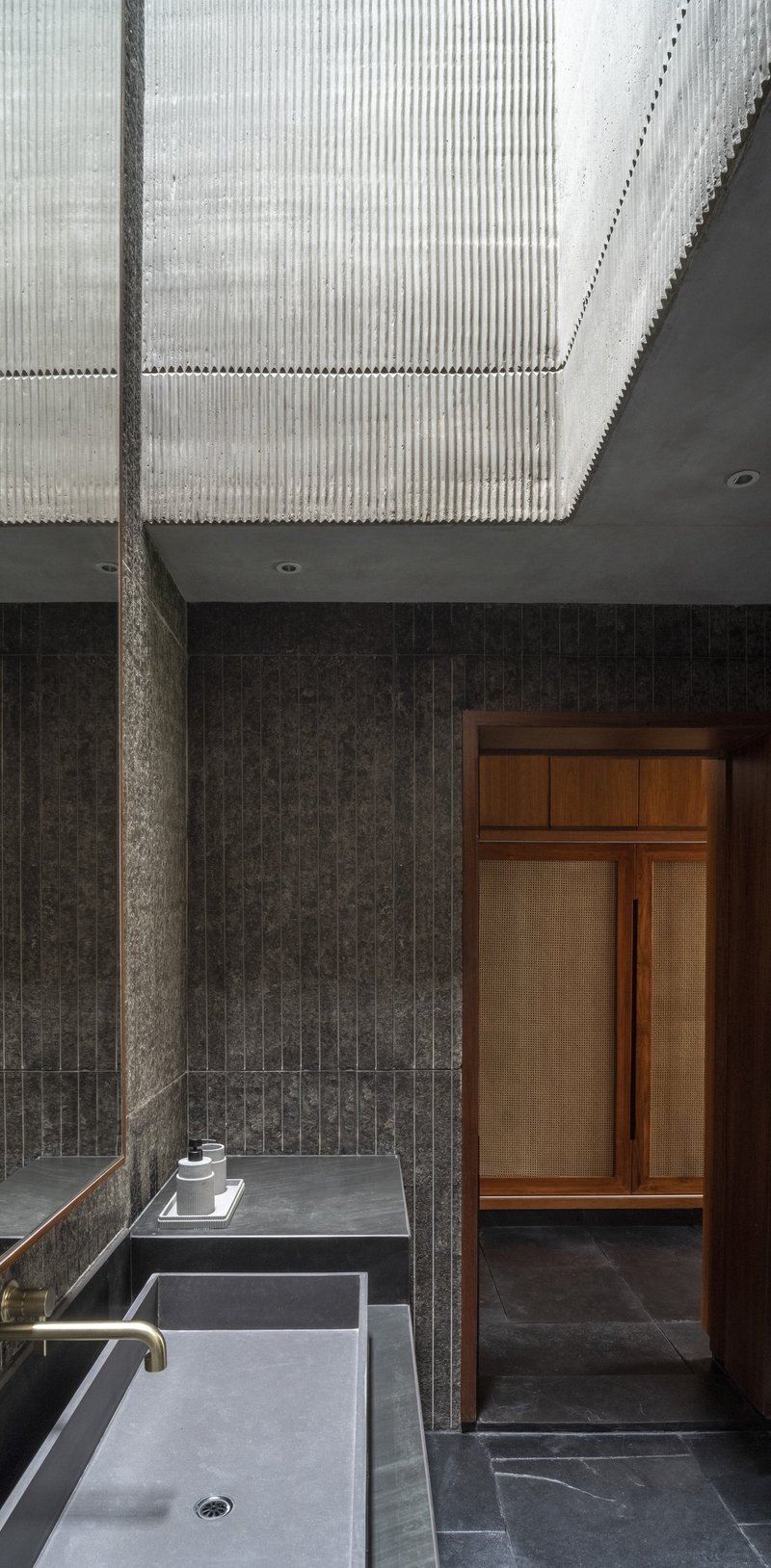 Bathroom with ribbed concrete ceiling above dark brick walls and a sunken grey stone bathtub