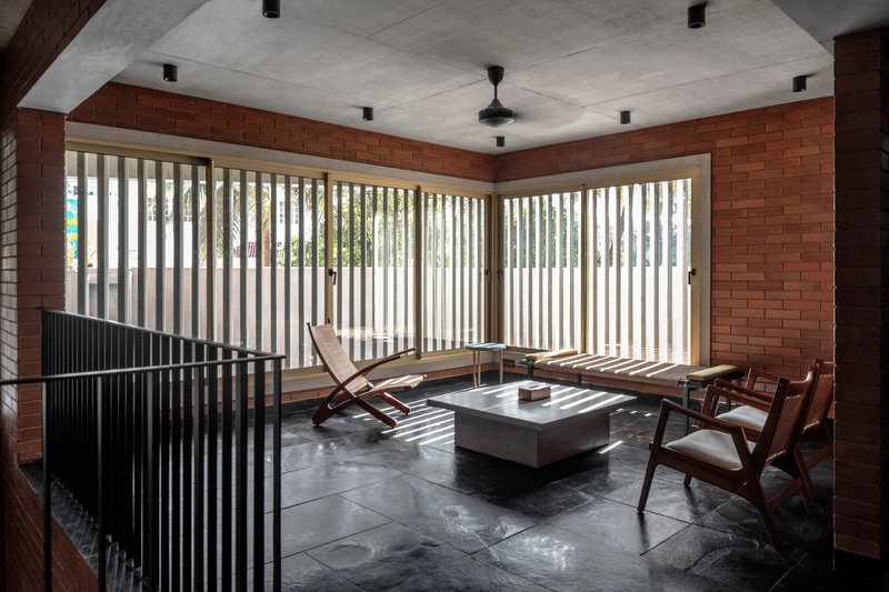 Living room with vertical timber louvres filtering daylight across brick walls and dark stone flooring