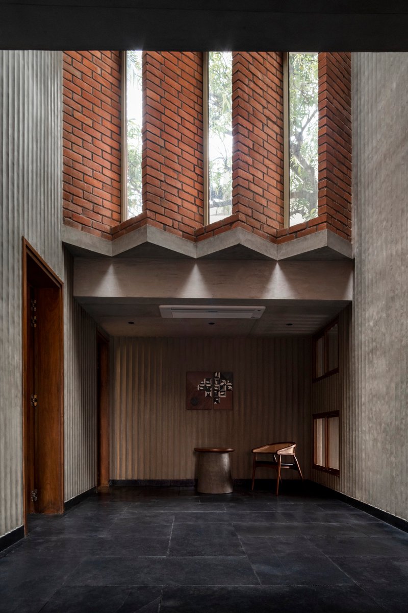 Double-height entry foyer with zigzag brick clerestory windows and concrete beams over dark stone flooring