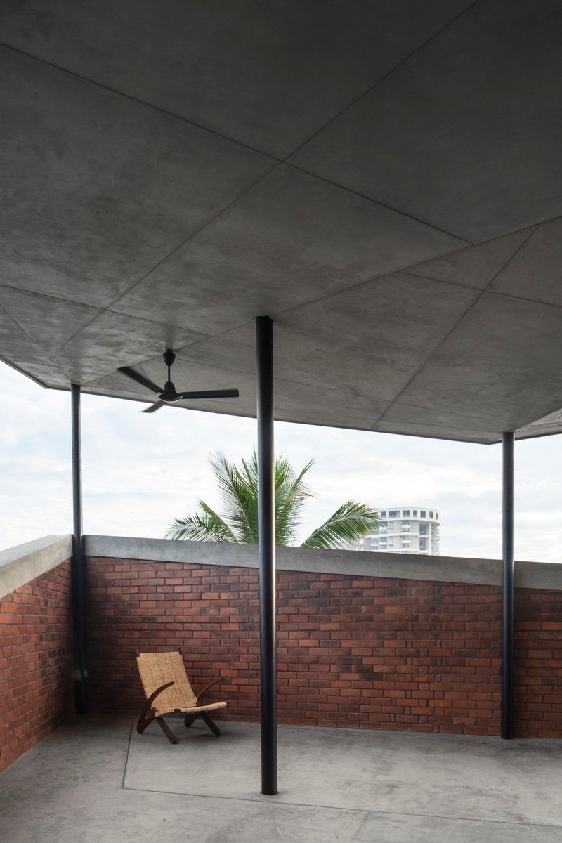 Rooftop terrace with concrete soffit, ceiling fan, steel columns, and brick parapet walls with palm fronds visible beyond