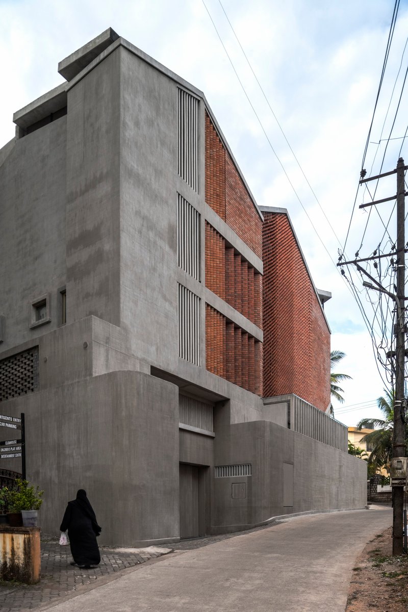 Street view of concrete and brick facade with vertical louvres and overhead power lines as a figure walks past