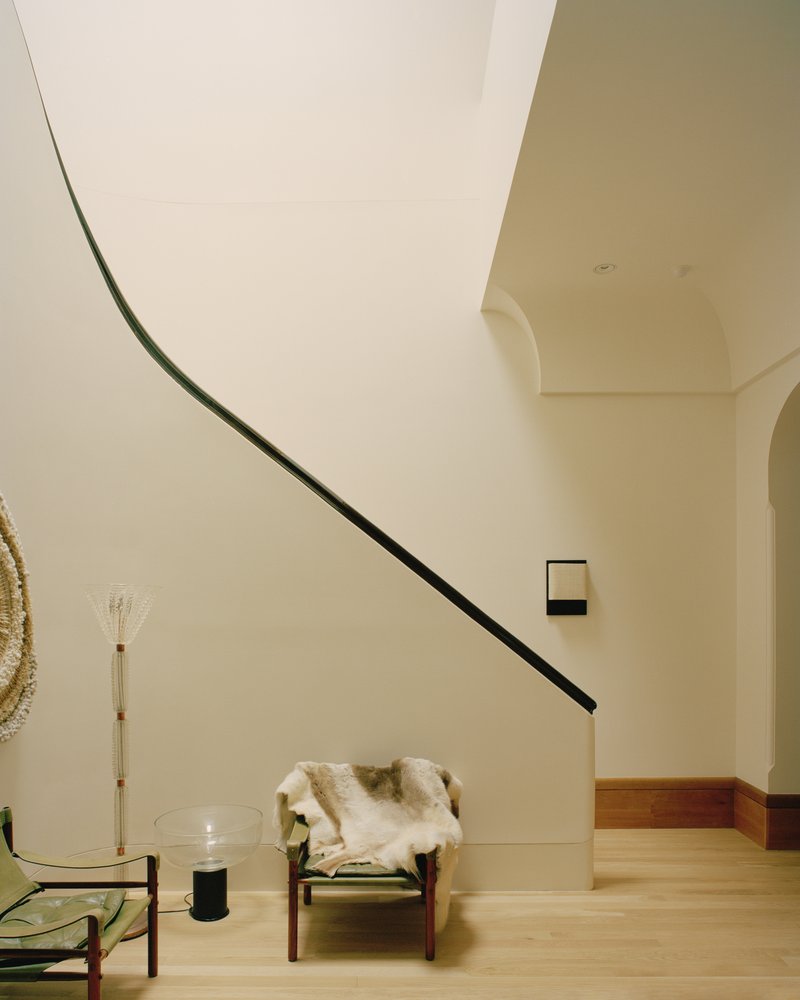 Curved staircase with black handrail ascending past pale walls and an arched opening in oak flooring