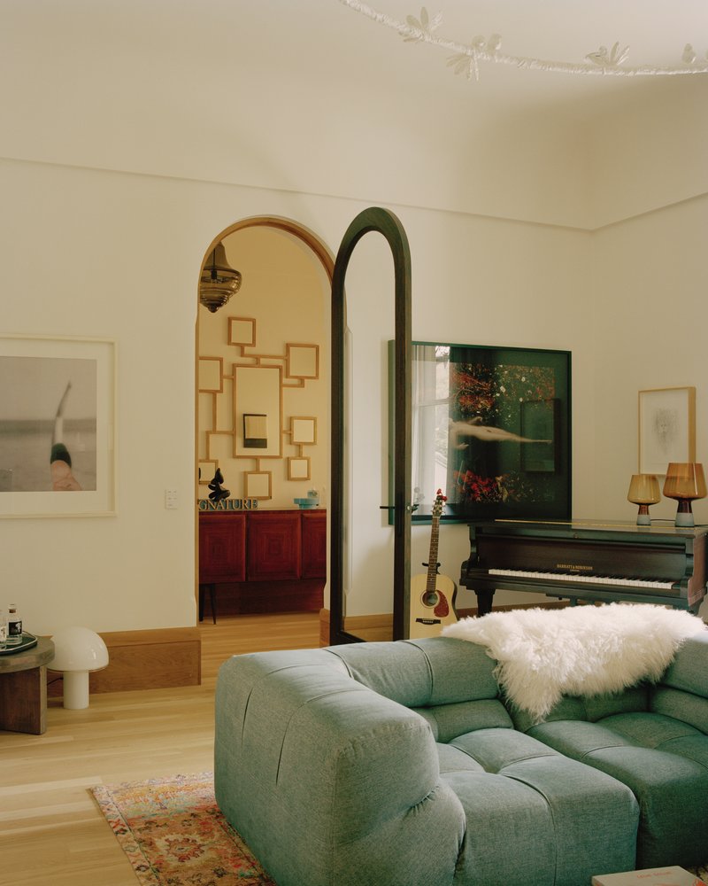 Living room with arched doorway framing a view through to an adjacent room with piano and artwork