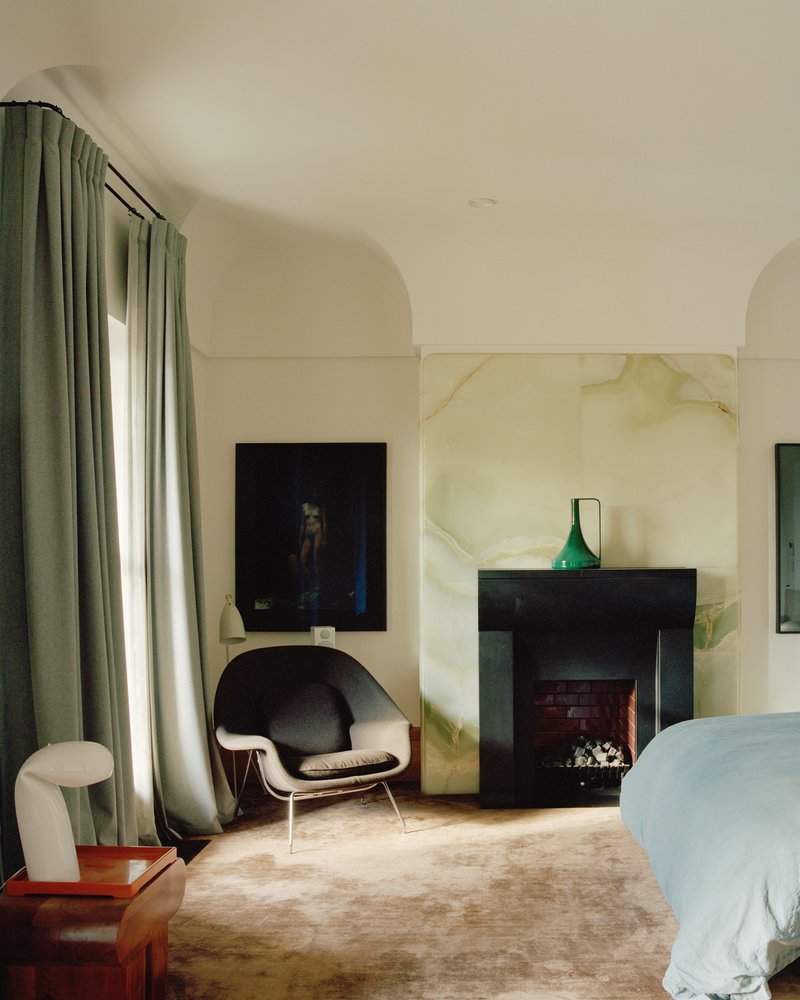 Bedroom with black fireplace surround against veined marble panel beneath arched ceiling and green curtains