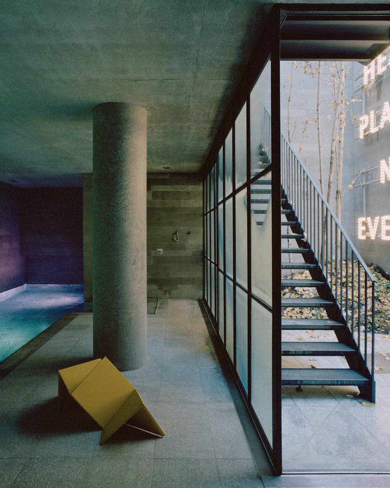 Open steel staircase beside floor-to-ceiling gridded window wall overlooking trees in daylight