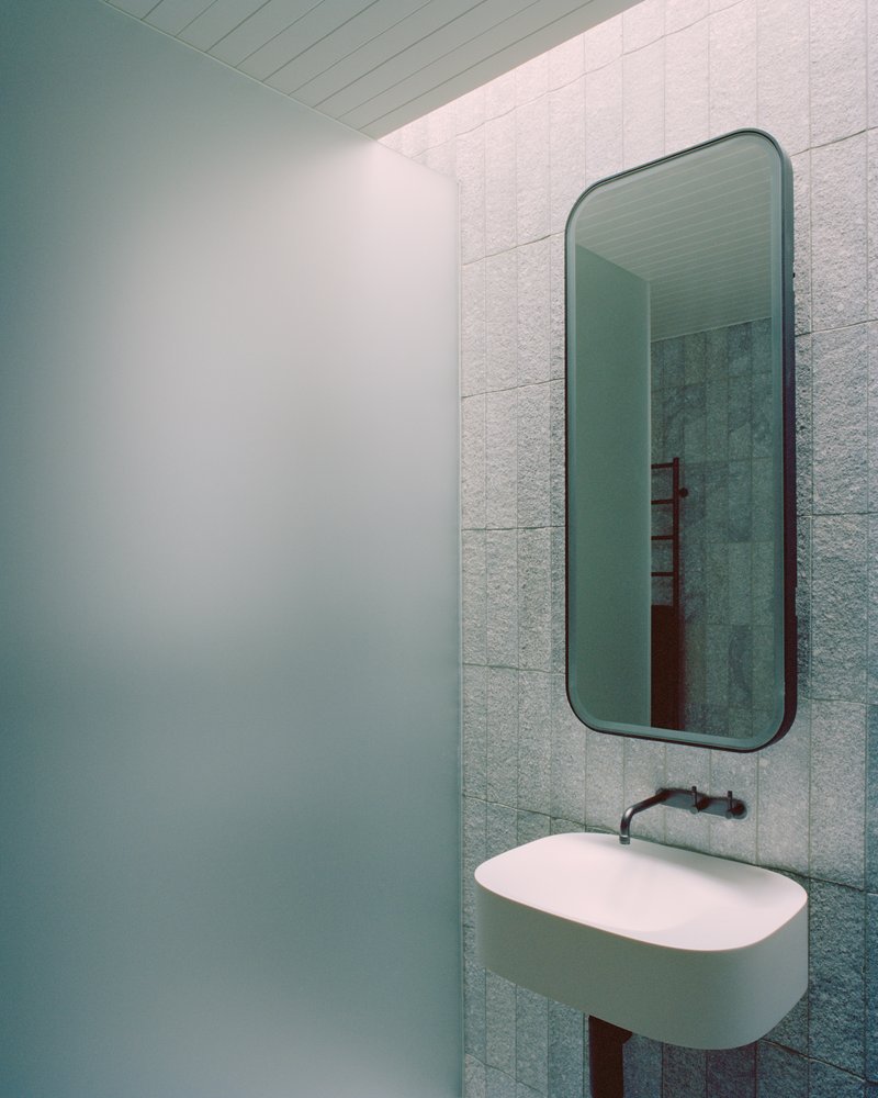 Bathroom corner with rounded mirror above floating sink and pale green tile cladding
