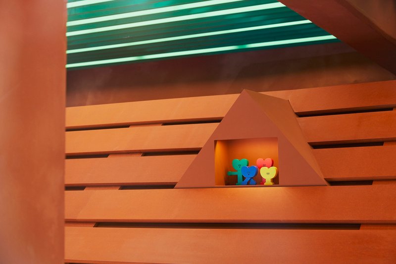 Triangular recess in horizontal wood slat wall with colorful objects under green striped ceiling
