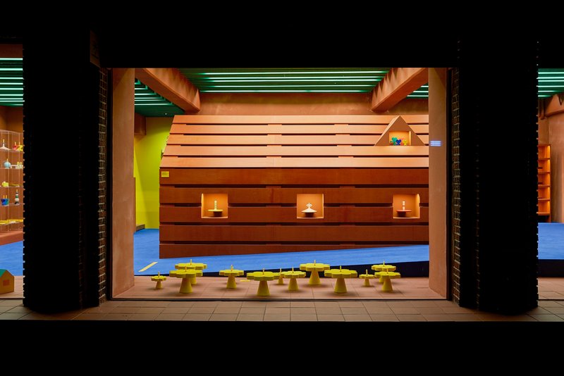 Horizontal wood-clad volume with square window cutouts and candles, flanked by black brick columns at night