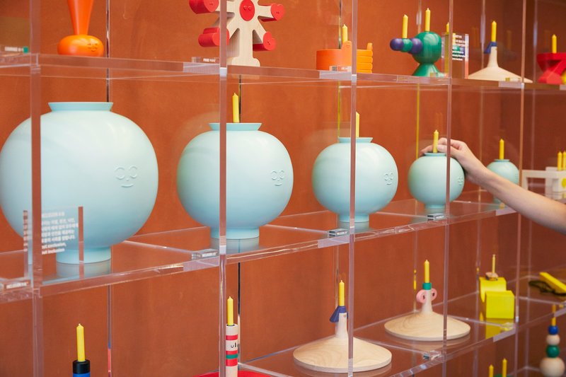 Transparent acrylic shelving displaying white ceramic vessels and candleholders with a hand reaching in