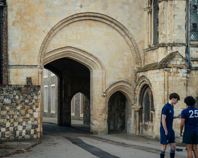Stone arched gateway framing a view of the flint facade with two students standing outside
