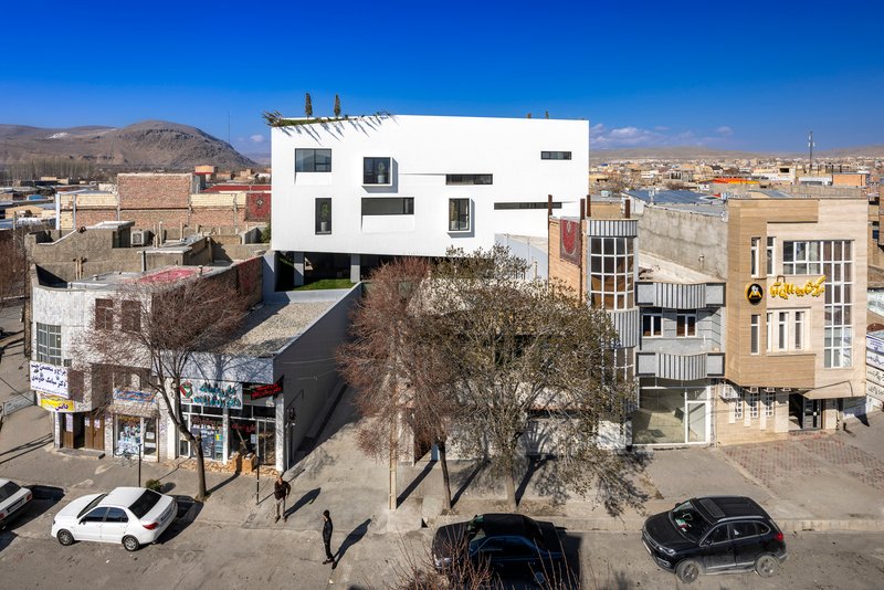 White cubic volume elevated above a dark base with bare winter trees in an arid townscape