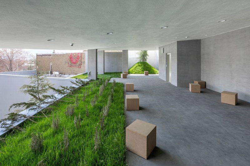 Covered terrace with planted grass strip and cube seating along a polished concrete floor