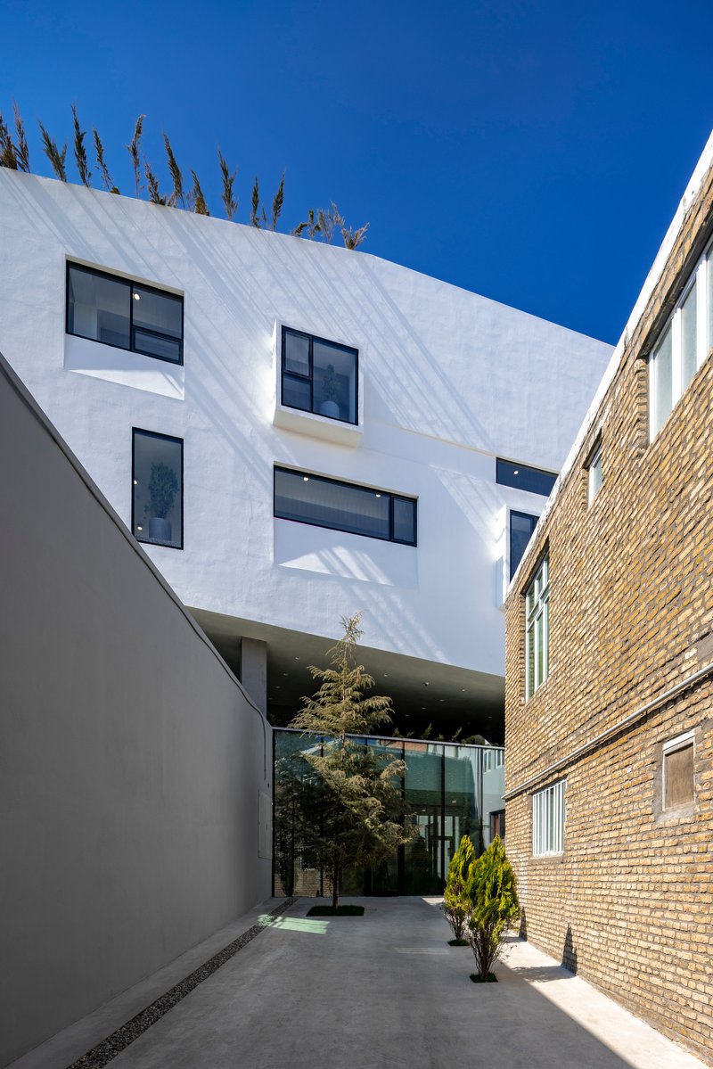 Narrow courtyard between white stucco facade and brick walls with planted trees and paved ground