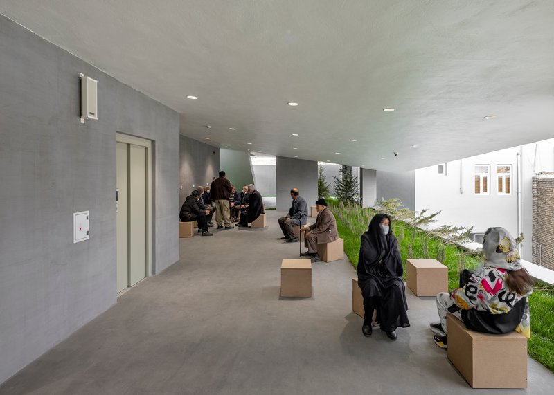 Interior gathering space with concrete walls, planted courtyards and people seated on cardboard cube benches