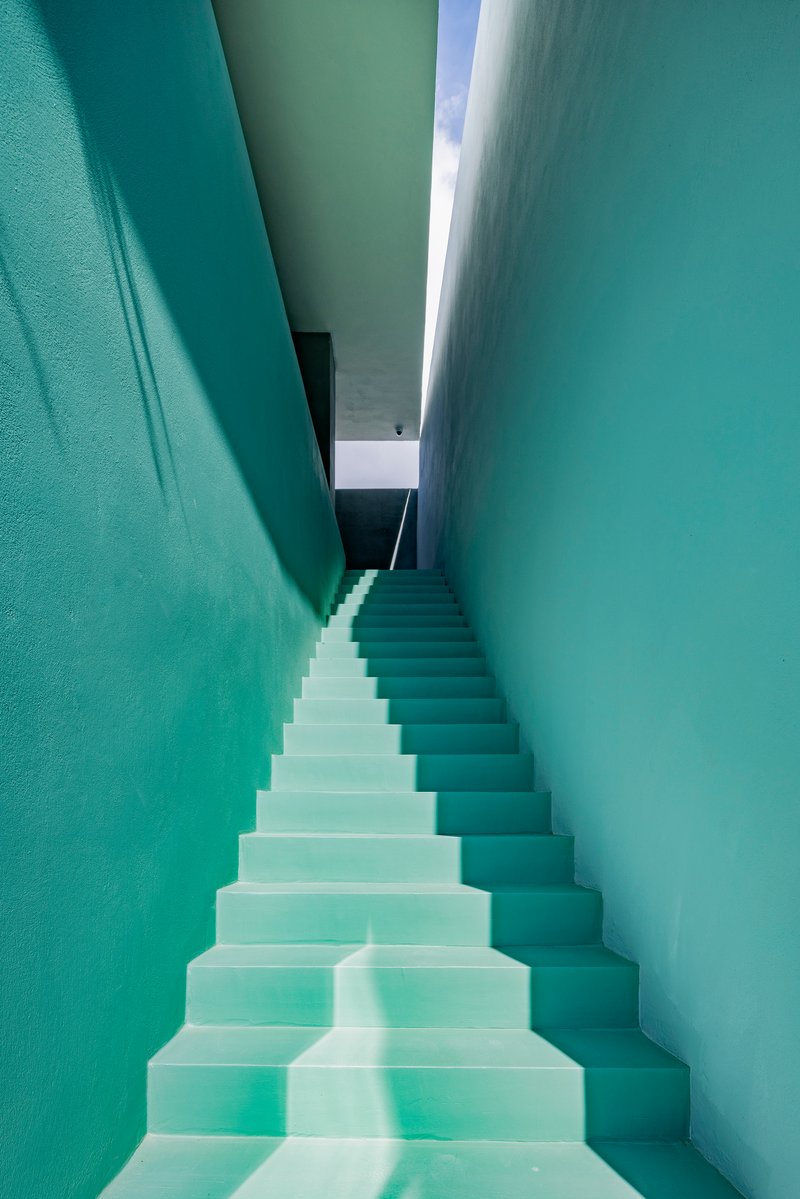 Narrow stairwell with mint green walls and skylight above casting light down the white treads