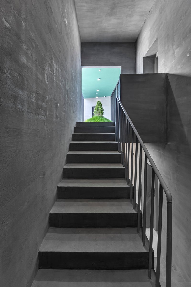 Concrete staircase with metal railing ascending toward a turquoise ceiling and glimpse of greenery