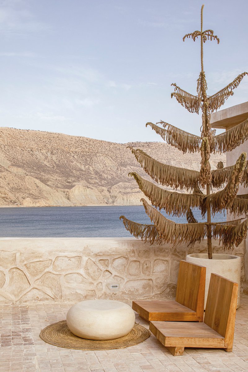 Terrace with decorative rope sculpture on pole beside stone seat wall overlooking water and hills