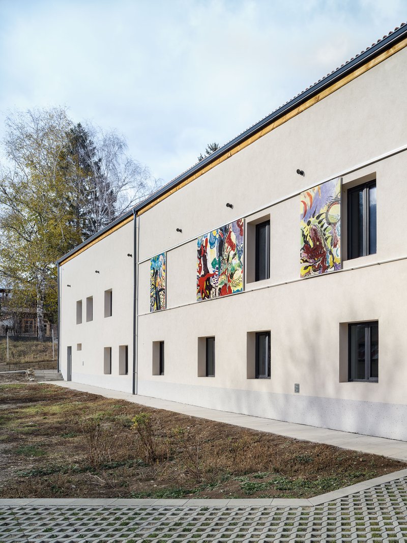White rendered facade with punched windows and four framed artworks under an overcast sky