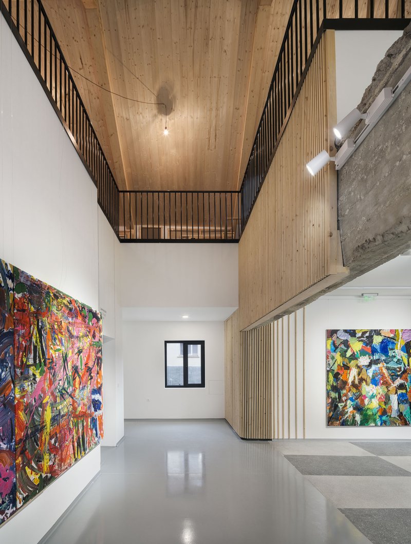 Double-height gallery space with timber slatted mezzanine and artworks hung on white walls