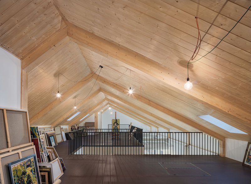 Attic storage area with exposed timber plank ceiling and metal railing overlooking gallery below
