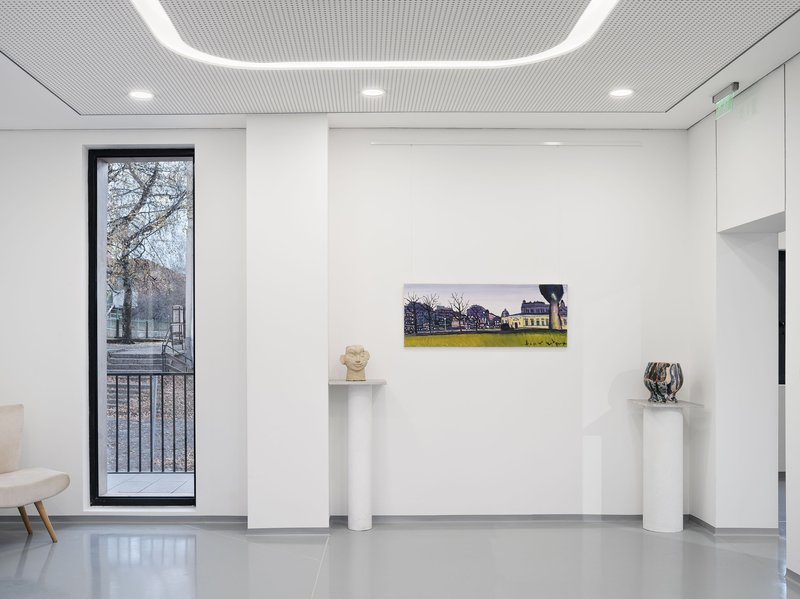 White gallery room with perforated metal ceiling, tall window framing bare winter trees outside
