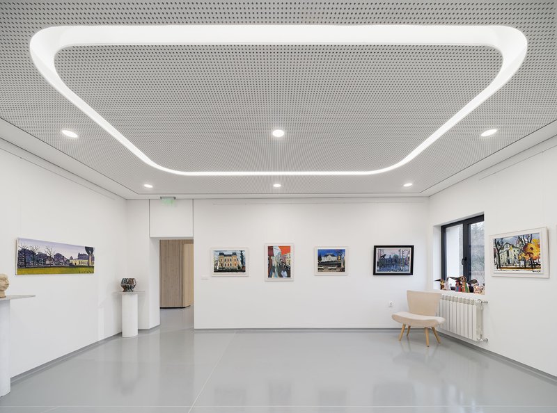 Gallery space with white walls displaying framed artworks and a curved linear ceiling light